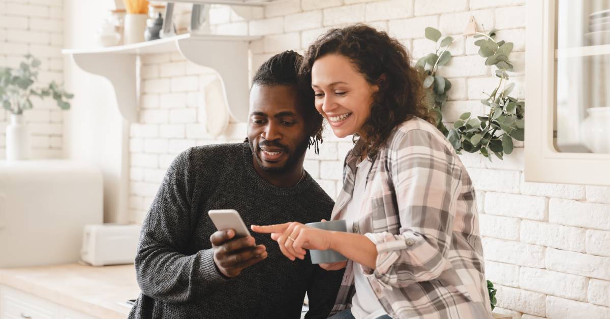 A middle-aged African American couple is sitting in the kitchen and looking at the man's phone together.