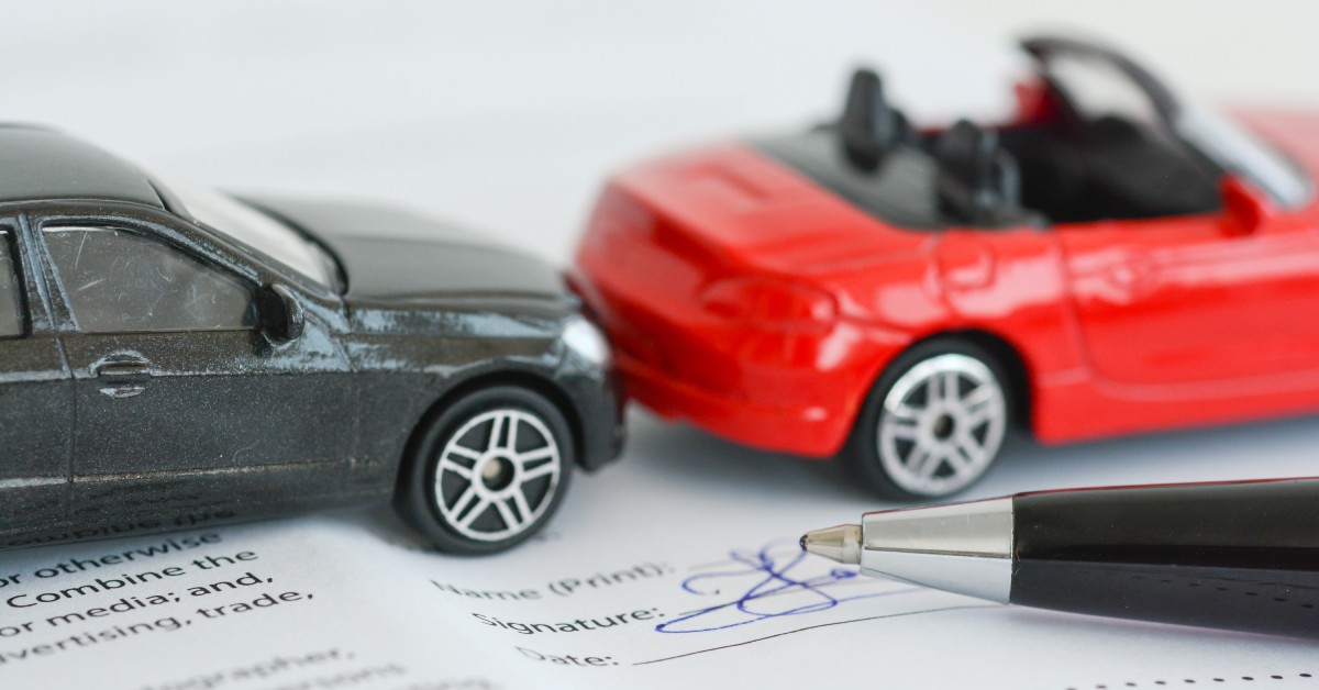 A model of a car accident using two toy cars, red and black, on top of an insurance Insurance policy contract.