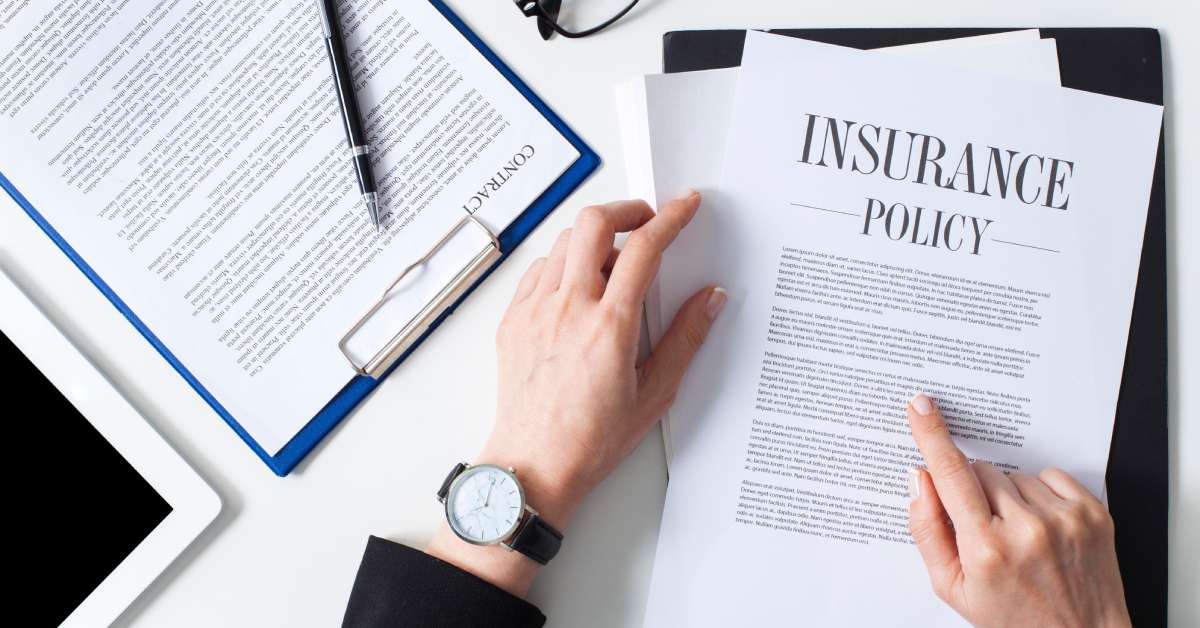 A businesswoman's hands hold and gesture to a paper reading 'insurance policy' next to a clipboard and glasses.