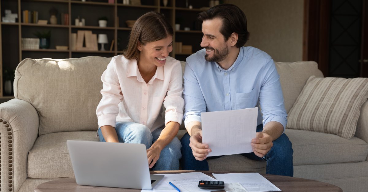 A man and woman sitting on a couch with a laptop and paperwork on a coffee table reviewing insurance policies.